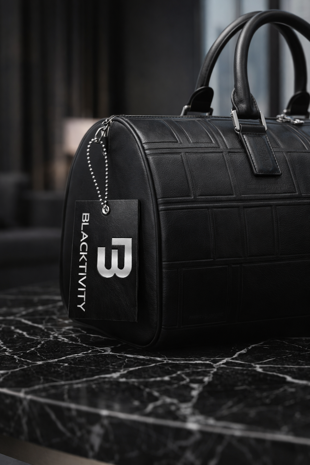 Black leather duffel bag with 'Blacktivity' brand tag on a dark surface